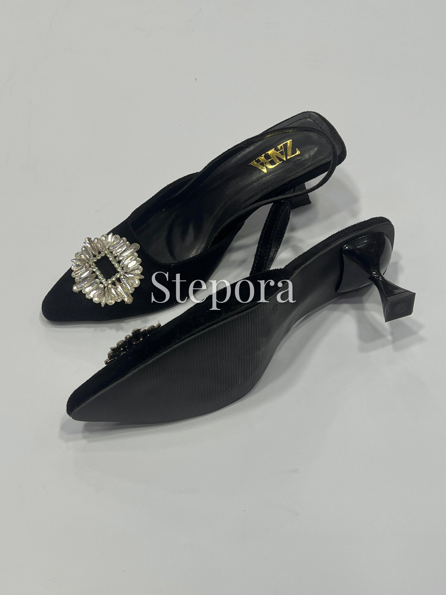 Black high-heeled shoes with a decorative brooch on a light gray background, featuring the brand 'Stepora'.
