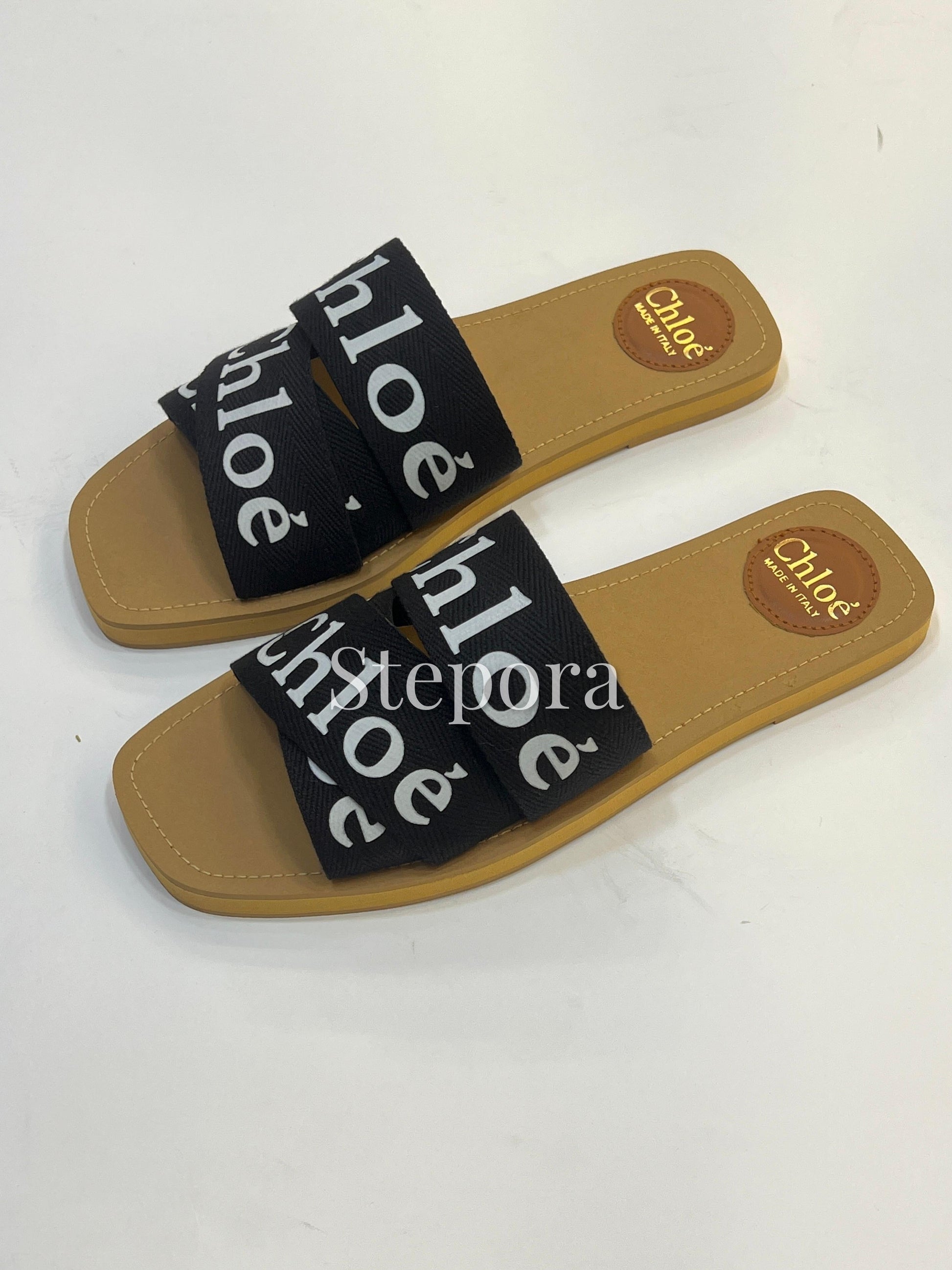 Pair of tan sandals with black straps featuring 'Chloé' branding on a white background.